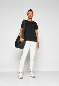 Juodas medvilninis marškinėlis, baltos sportinės kelnės su šoniniais akcentais ir pilkai baltos sportbačiai. Juoda kuprinė su petnešomis. Paprastas sportinis dizainas.