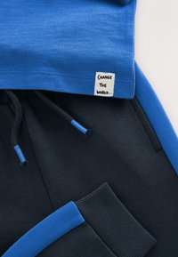 Sinine puuvillane T-särk, kantud tumeda halli puuvillase dressipükste kohal. Märkimisväärsed omadused hõlmavad kangasildiga "CHANGE THE WORLD" ja siniseid aktsente.