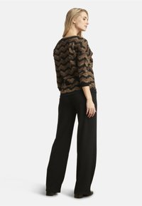 Black and gold zigzag patterned top with three-quarter sleeves, paired with black wide-leg pants. Made from soft, textured fabric.