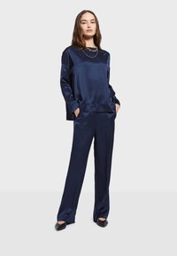 Granatowy satynowy zestaw dresowy, składający się z luźnej bluzki z kieszeniami oraz spodni w prostym kroju. Gładka tekstura z delikatnym blaskiem.