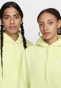 Due persone indossano felpe di un brillante verde lime con tasche frontali e cordini. Il logo Nike è visibile sul petto di ciascuna felpa.