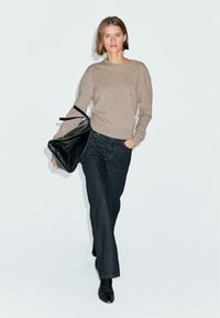 Maglione lavorato a maglia beige, jeans dritti blu scuro e borsa in pelle nera. Texture liscia con dettagli hardware minimi. Design semplice.