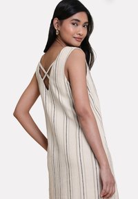 Helles beige ärmelloses Kleid mit vertikalen Streifen, V-Ausschnitt am Rücken und überkreuzten Trägern. Hergestellt aus einem strukturierten Stoff.
