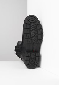 Schwarze Lederstiefel mit einer strukturierten Gummisohle, die ein robustes Profildesign aufweist. Das Etikett trägt die Aufschrift "Hergestellt in Italien", Größe 37 ist an der Seite eingestanzt.