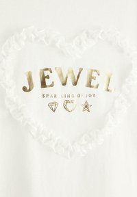 Vit t-shirt med guldtexten "JEWEL SPARKLING OF JOY," omgiven av ett veckat, transparent hjärta med diamanter och stjärnor.