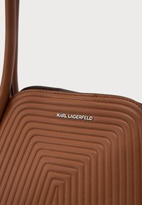 Mala crossbody de couro marrom, com padrão geométrico em relevo e logótipo prateado de Karl Lagerfeld na parte da frente.