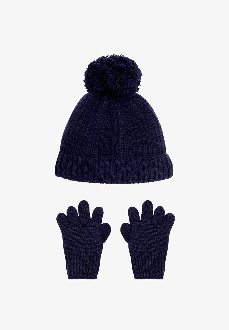 Tamsiai mėlynas megztas kepurė su pom-pomu viršuje ir įrėmintu tekstūra, derinamas su atitinkamomis pirštinėmis, turinčiomis keturis pirštus ir nykštį.