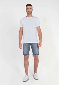Witte korte mouwen T-shirt gecombineerd met lichtblauwe denim shorts met opgerolde boorden. Witte sneakers met lichtbruine zolen. Casual outfit.