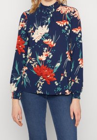 Blommig blus i marinblått med röda och rosa blommor, samlad halsringning, långa ärmar och elastiska manschetter, tillverkad av lättviktsmaterial.