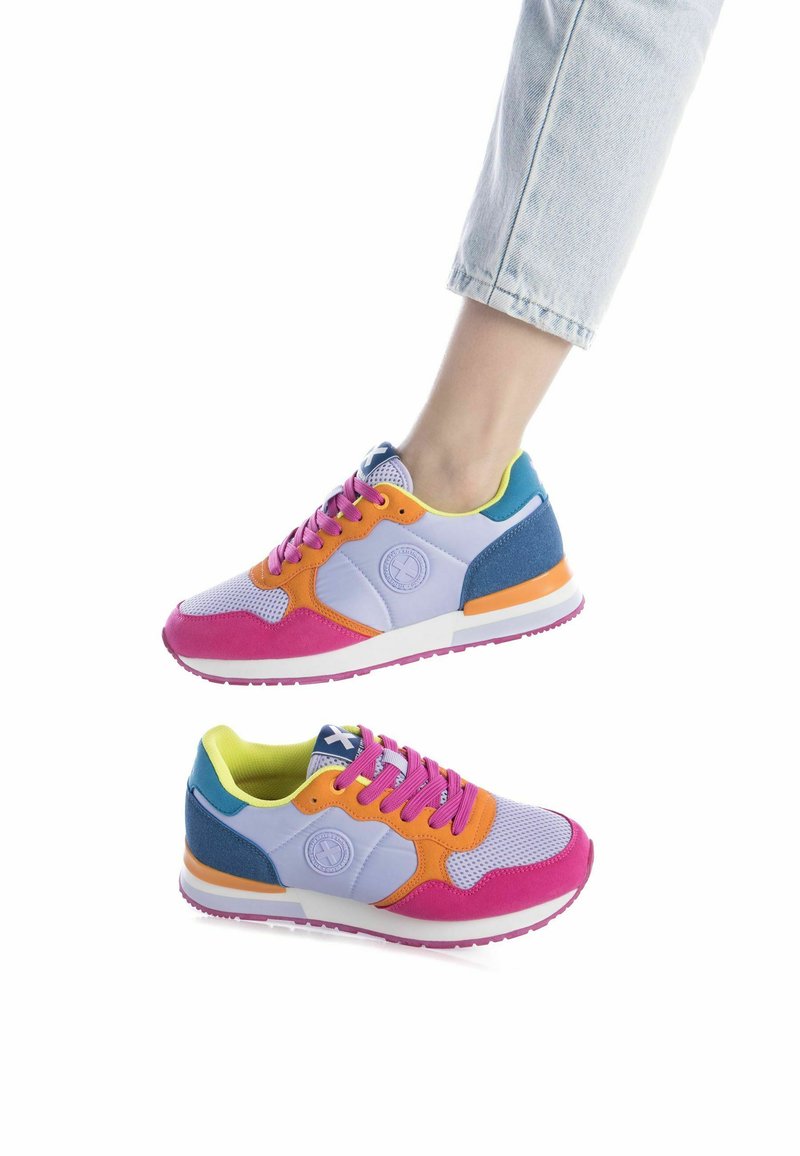 Zapatillas coloridas con una mezcla de materiales morados, rosas, naranjas y azul verdoso. Presentan paneles de malla, un collar acolchado y suela de goma.
