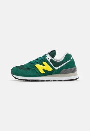 Zielono-biały sneaker New Balance z żółtym logo, szarym wsparciem pięty i czarną podeszwą widziany z boku na białym tle.
