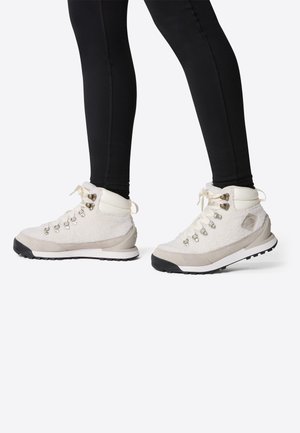 Scarponi da trekking con tomaia in materiale peloso color crema, dettagli in pelle beige e suole in gomma nera. Presentano occhielli metallici e lacci.