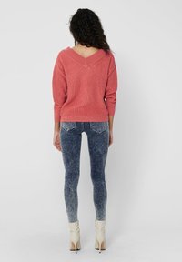 Roze gebreide trui met een V-hals ontwerp, gecombineerd met vervaagde blauwe skinny jeans en beige hakken. Gelaagd stof en aangesloten silhouet.
