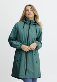 Jachetă verde rezistentă la apă, cu fermoar frontal, mansete elastice și glugă ajustabilă. Are două buzunare laterale și un design de lungime medie.