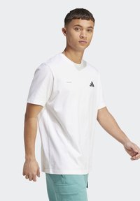 Hvid bomulds t-shirt med rund hals, korte ærmer og et lille sort Adidas-logo på brystet, båret med aqua-farvede bukser.