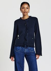 Marineblauer strukturiert Cardigan mit fransigen Kanten, Rundhalsausschnitt und Fronttaschen; mit goldfarbenen Knöpfen für Details. Kombiniert mit Jeans.