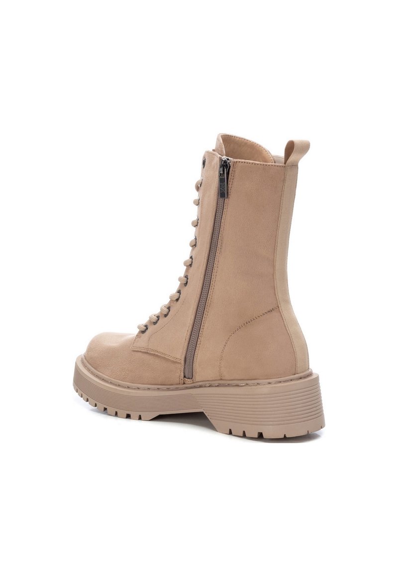 Botín de ante beige con cordones en la parte delantera, cremallera lateral y suela de goma gruesa. Presenta una lengüeta y detalle de costura texturizada.