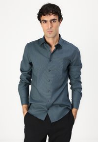 Chemise à manches longues boutonnée en bleu canard foncé avec des motifs géométriques subtils, dotée d'un col classique et de boutons noirs.