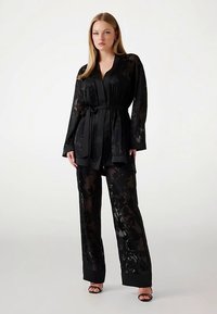 Set in tessuto trasparente nero con motivo floreale, composto da top stile avvolgente, maniche lunghe e pantaloni abbinati, con cintura e design a gamba larga.