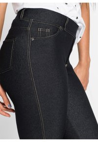 Czarne dżinsy z wysokim stanem, z kontrastującym złotym ściegiem, gładką teksturą i dopasowanym krojem podkreślającym tylne kieszenie.