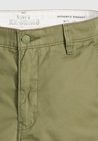 Pantaloni Chino Levi's XX, verde măsliniu, fabricați dintr-un material de bumbac neted. Prezintă o croială dreaptă autentică, cu închidere cu buton și detalii cusute.