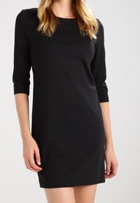 Svart, figurnära klänning med trekvartslånga ärmar. Tillverkad av ett glatt tyg, har rund halsringning och en minimalistisk design.