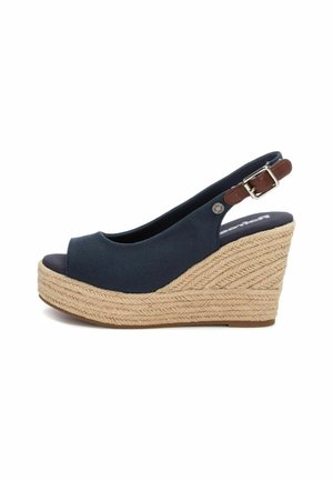 Zapato de cuña tipo slingback en tela azul oscuro con punta redondeada y abierta, que cuenta con una plataforma de cuerda natural trenzada y una pequeña hebilla marrón.