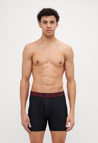 Boxeri negri, cu un logo roșu "Under Armour" pe talie. Materialul pare neted și elastic, proiectat pentru confort și potrivire.