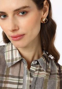 Gold hoop earrings with geometric accents, worn with a checkered blouse featuring shades of gray, white, and green. Smooth texture, button detail.