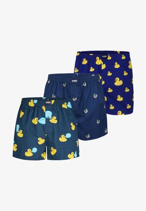 Tre par blå boxershorts med gule mønstre af gummidue og gråand, hver i varierende blå nuancer og andedesign.