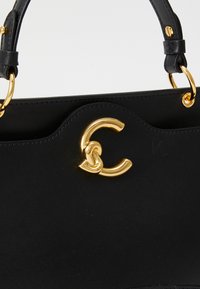 Black leather handbag featuring a prominent gold C-shaped logo, structured design, and a smooth texture with gold hardware accents.