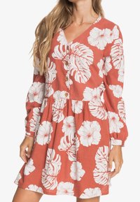 Czerwona sukienka z białymi kwiatowymi wzorami, z dekoltem w szpic, długimi bufkami i drewnianymi guzikami z przodu. Projekt spódnicy w kształcie dzwonu.