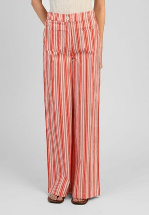 Femme portant un pantalon taille haute à jambes larges avec des rayures verticales rouges, orange et beige et des poches plaquées devant, associé à des sandales à bout ouvert.