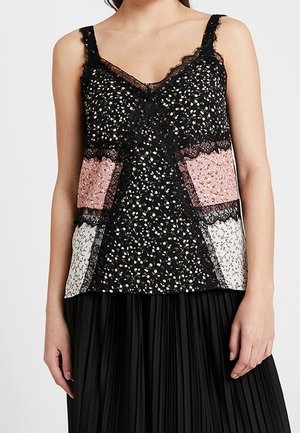 Haut sans manches à col en V avec des panneaux floraux noirs, roses et blancs et une bordure en dentelle noire, porté avec une jupe plissée noire.