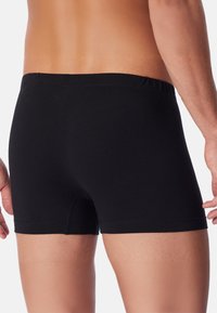 Boxer in cotone nero con vita elasticizzata. Il tessuto è liscio e aderente, con una lunghezza che arriva a metà coscia.