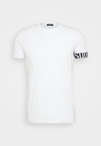 Weißes T-Shirt mit kurzen Ärmeln aus Baumwolle, versehen mit einem schwarzen gestreiften Band am linken Arm, auf dem das Wort "INST." gedruckt ist.