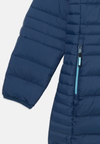 Tumesinine puhvjakas horisontaalse õmblusega, millel on helesinine lukuga tasku. Pehme, tikkimisviisiga materjal ja soonikud varrukatel.