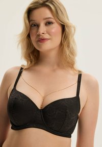 Czarny stanik z teksturowanym kwiatowym wzorem, z fiszbinami i regulowanymi ramiączkami. Posiada delikatny złoty łańcuszek na dekolcie.