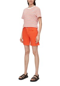 T-shirt à rayures rouges et blanches à manches courtes associé à un short en denim orange vif, complété par des sandales noires à plusieurs lanières.
