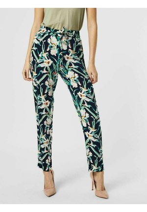 Slim-fit pants with dark background and white floral print worn with beige high heels and light olive green tucked-in top.