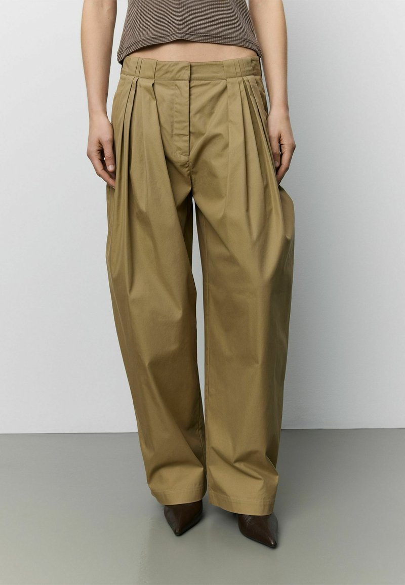 Personne portant un pantalon ample taille haute beige avec des plis, associé à un haut court marron côtelé et des chaussures brunes foncées pointues.