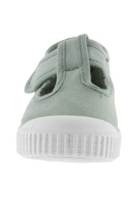 Scarpa in tela verde con punta arrotondata, suola in gomma bianca e dettagli laterali ritagliati. Presenta una fascia a strappo per una calzata sicura.