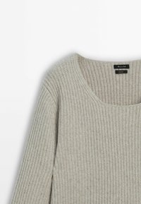 Pull en laine beige à côtes avec manches longues et encolure dégagée, présenté sur un fond blanc.