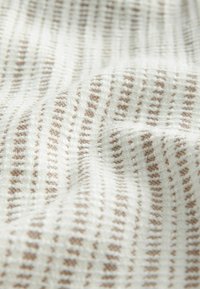 Wit gestructureerd textiel met afwisselend bruine strepen, voorzien van een zacht, geweven patroon dat diepte en visuele interesse creëert.