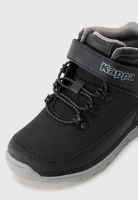 Botas de exterior negras con parte superior sintética texturizada, sistema de lazada, acolchado en el collar y suela de goma gris. La marca es visible en el lateral.