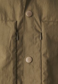 Olive green jacket featuring a textured fabric, two front pockets, and metallic buttons. Includes zippers for adjustable fastening.