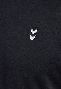 Zwarte stoffen t-shirt met een wit chevronlogo op de bovenste linkerkant. Glad textuur met een nauwsluitend ontwerp.