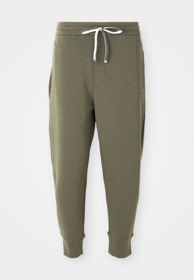 Olivenfargede joggebukser med hvit snor, elastisk midje, sidelommer og ribbede mansjetter på hvit bakgrunn.