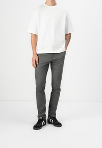 T-shirt bianca a maniche corte, pantaloni slim-fit grigi e sneakers nere con strisce bianche. Tessuto morbido con una vestibilità rilassata e design semplice.