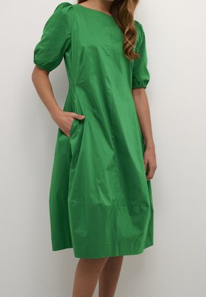 Robe en coton verte avec des manches à volants, longueur genou, poches latérales, texture lisse et encolure ronde. Aucun motif ni embellissement visible.